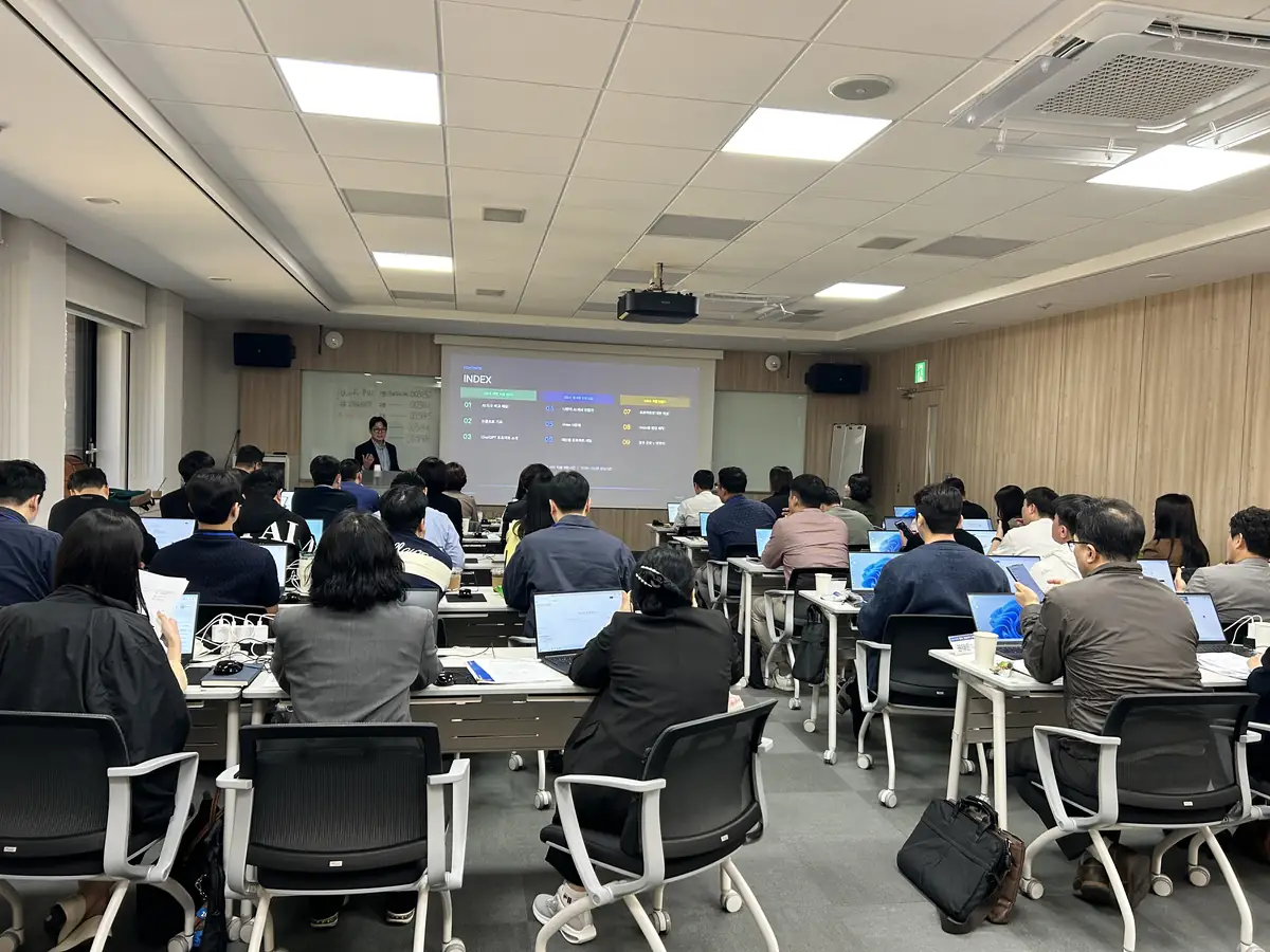 기업 임직원들이 노트북으로 실습하고 강사가 앞에서 화면을 보며 설명하는 AI 교육 현장
